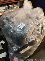 Large clear plastic bag filled with multiple skeins of dark and neutral toned yarn, sealed