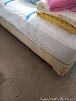 Photo showing used queen mattress with foam padding and folded blanket on top, sitting on box spring and bed frame.