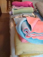 Stack of colorful wool blankets in pink, blue, yellow, and green stacked on bed along with foam mattress pad and mattress cover