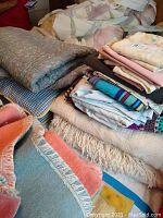 Overview of stacked bedding items including blankets, sheets, and pillowcases in various colors and patterns.