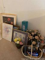 Framed floral and doorway scene wall art grouped against wall along with Galileo thermometer box and artificial floral arrangements in vases.