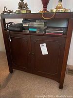 Front view of vintage wooden side table with glass top and closed cabinet doors. Some scratches visible on wood surface.