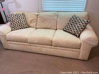 Front view of beige three-cushion sofa with two patterned pillows on each arm, showing upholstery and condition.