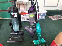 Three vacuums including black Fantom Danton upright vacuum, purple/yellow Bissell PowerLifter upright vacuum, and teal cordless Swiffer mop.