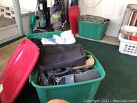 Three large green totes filled with men's clothing and shoes, with some clothing visible on top and around the totes