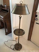 Full view of brass floor lamp with conical shade, integrated round end table, and double pull chains.