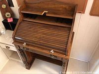 Front view of the roll top desk showing the closed slatted roll cover, central drawer with metal handle, and cubby compartments under the top shelf.