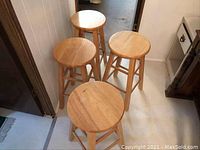 Photo showing four solid wood stools arranged on floor with natural wood finish and round seats.