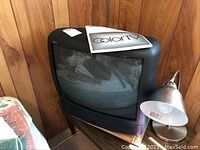 Front view of RCA 20 inch CRT TV showing screen and instruction manual on top, placed against wooden paneled wall with a lamp nearby.