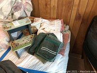 Photo of vintage painted wooden two-step stool with sunflower and farm animal designs along with assorted linens including towels and tablecloths around it.