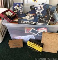 Overview photo showing various sports magazines and books, primarily Tampa Bay Lightning hockey, inside a laundry basket with some vintage memorabilia boxes.