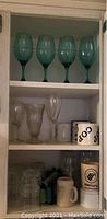Multiple shelves with assorted glassware including clear drinking glasses, coffee mugs, and other glass items.