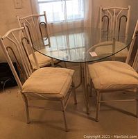 Round glass top table with four white metal chairs arranged around it in dining room setting.