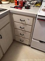 Four drawers of a light wood cabinet with black handles containing flatware and kitchen items