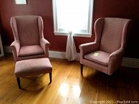 Pair of wing chairs with matching footrest in a room with wooden floors. Chairs and footrest covered in red and tan checked fabric slipcovers, showing some fading.