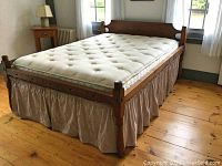 View of complete bed with mattress and bedskirt, set on wooden floor with side of room windows visible.