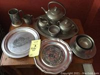 Photo of 12 pewter items including decorative plates, tea set, tray and other small pieces