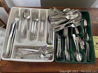 Full view of mixed flatware in two trays showing forks, knives, spoons, and iced tea spoons with multiple handle patterns.