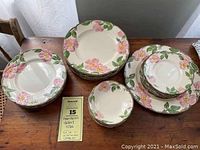 Full set overview arranged on table showing stacks of plates and bowls with floral design and scalloped edges.