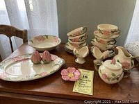 Full set arranged on wooden table showing six cups and saucers stacked, oval platter with salt and pepper rose bud shakers, teabag holder, sugar bowl with lid, creamer and a pair of candlesticks, along with an 8 inch flower bowl.