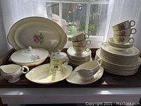 Full set displayed on window sill including stacked plates, cups, serving dishes with visible floral pink rose pattern and gold banding.