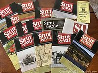 14 issues of Strut & Axle magazine laid out, showing various covers featuring transportation and museum themes.