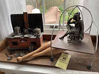 Photo showing vintage litho salesman sample stove with miniature pots and pans, plate, and utensils on wooden base along with pot metal figurine on metal platform with wire frame structure above