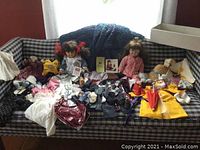 Wide view of two dolls, historical outfits, sports uniform and accessories spread on couch