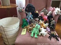 Photo showing a variety of Beanie Babies and other stuffed animals arranged on a red and white checkered chair, all with tags, including green bear, black poodle, blue dog, white rabbit, and pink pig, plus black spider and others.