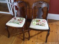 Pair of antique Empire style side chairs with burled wood frames and crewel work upholstered seats placed on wooden floor.
