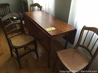 Full view of antique pine table with both leaves down, showing worn wooden surface and three cane seat chairs beside it.