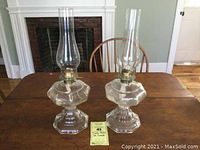 Front view of the pair of vintage glass oil lamps on a wooden table with fireplace background.