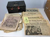 Photo showing black metal document box and spread of 1974 newspapers and 1800s magazines
