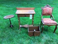 Photo of 4 vintage accent furniture pieces including a scalloped wood side table, a narrow wood table with drawer, an upholstered carved wooden chair, and a wooden magazine holder on grass.