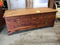 Full view of rectangular cedar chest with metal detail on front, resting on concrete floor.