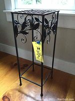 Full view of the metal plant stand in a room by a window showing the overall shape and design.