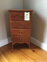 Full view of the small pine chest of drawers showing four drawers with wooden knobs and its height relative to floor and wall corner.