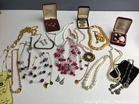 Full overview of costume jewelry including necklaces, earrings, pins, and watch laid flat on white surface.