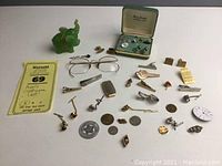 Overview of the entire lot showing assorted men's costume accessories including cufflinks, pins, coins, eyeglasses, and resin figurine.