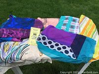 Nine vintage scarves arranged on outdoor surface showing various colors and patterns including solid purple-blue with polka dots and stripes.