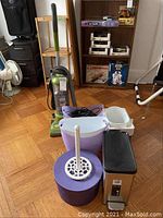 Photo showing the vacuum cleaner, plastic buckets, toilet brush holder and step trash can on a hardwood floor.