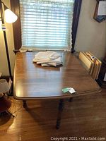 Wooden double drop leaf dining table placed near window with light-colored curtains, viewed from above and side angles.