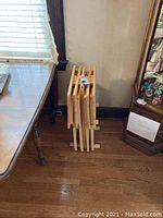 View showing three wooden folding TV trays stacked together with a light natural wood finish and foldable legs.