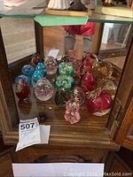 Glass paperweights displayed inside a wooden and glass cabinet, showing various colors and designs.