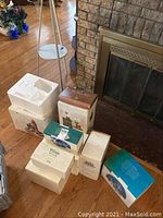 Multiple Department 56 house boxes stacked near fireplace. Boxes have various designs and are in different conditions.