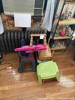 Wood and plastic step stools grouped together on wooden floor near radiator and shelving unit showing variety of materials, colors, and visible scratches.