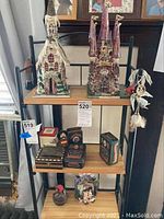 Two tall ceramic church-style figurines standing on a shelf above multiple decorative lidded tins with varied patterns