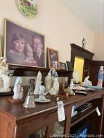 Photo showing various religious figurines, crucifixes, and a metal bell on a wooden mantel shelf under family photos.