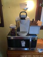 Emerson microwave with Keurig coffee maker, plastic storage container with reusable coffee pods, and an empty box on top of microwave.