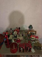 Table displaying Carlton Cards boxed ornaments, assorted figurines including polar bears and Santa, red and green candle holders, and other Christmas decorations piled together.